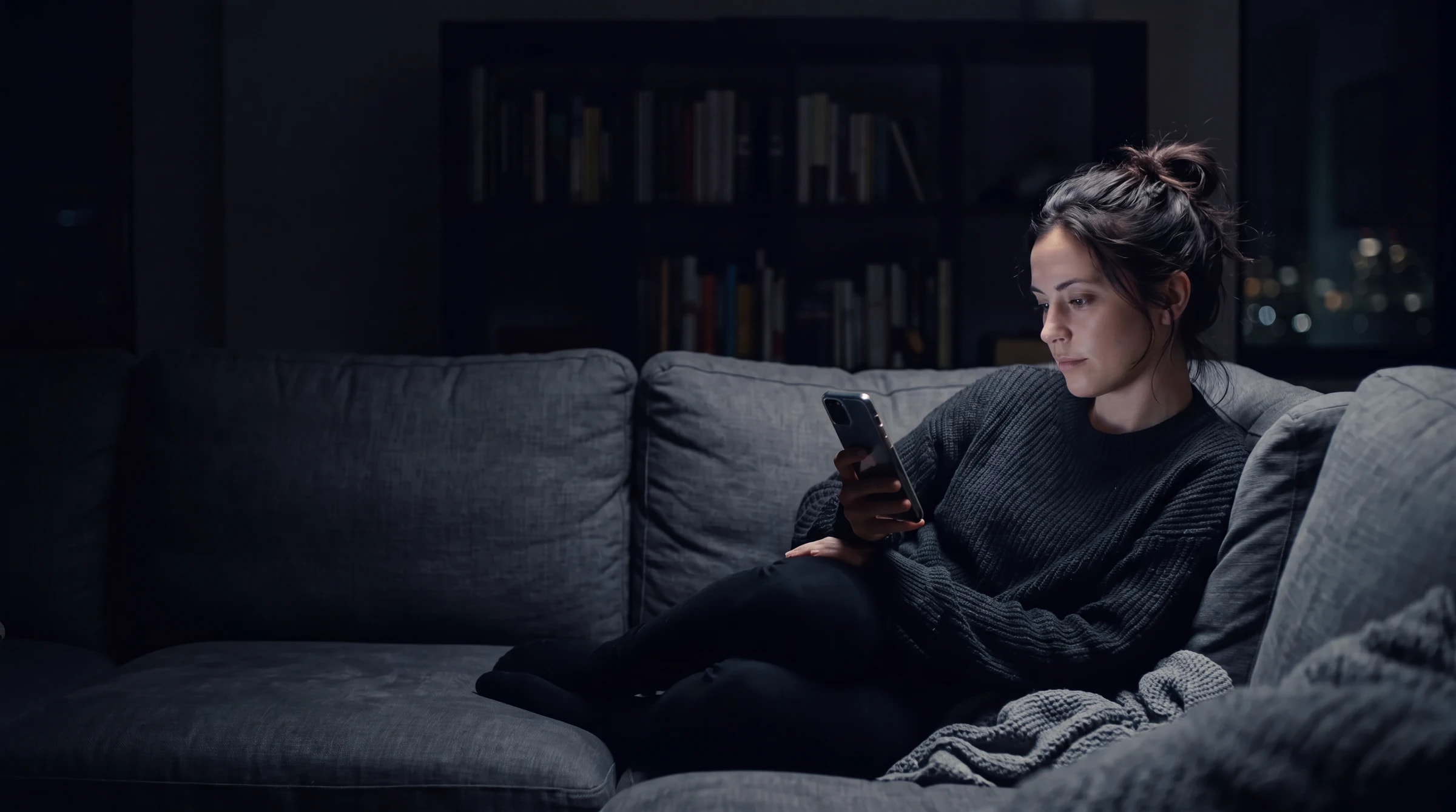 A shopper on a couch at night, browsing a store on her phone, her face lit by the screen